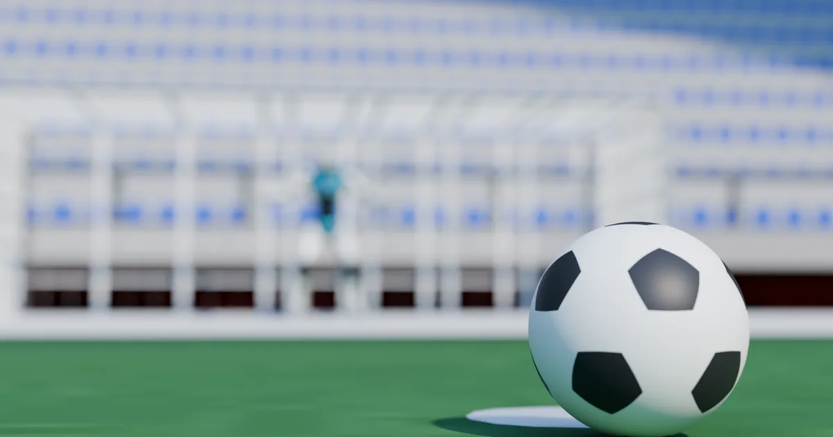 Le ballon sur le point de penalty, le gardien flou au fond.